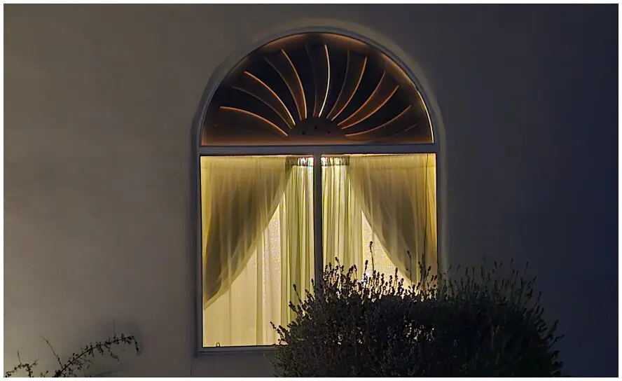 Arched window with illuminated curtains at night.